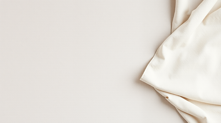 Soft pale greige linen laid flat in warm daylight, with a single fold at the right edge